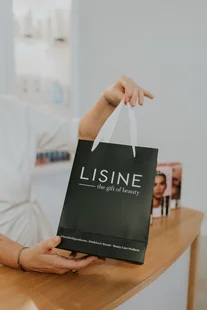 Hand met een zwarte LISINE-cadeautas boven een houten tafel
