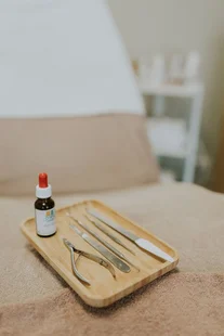 Houten schaaltje met pedicure-instrumenten en een druppelflesje op een behandeltafel