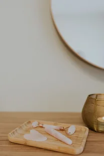 Houten schaaltje met witte gezichtsmassagetools naast een gouden kaarsenhouder