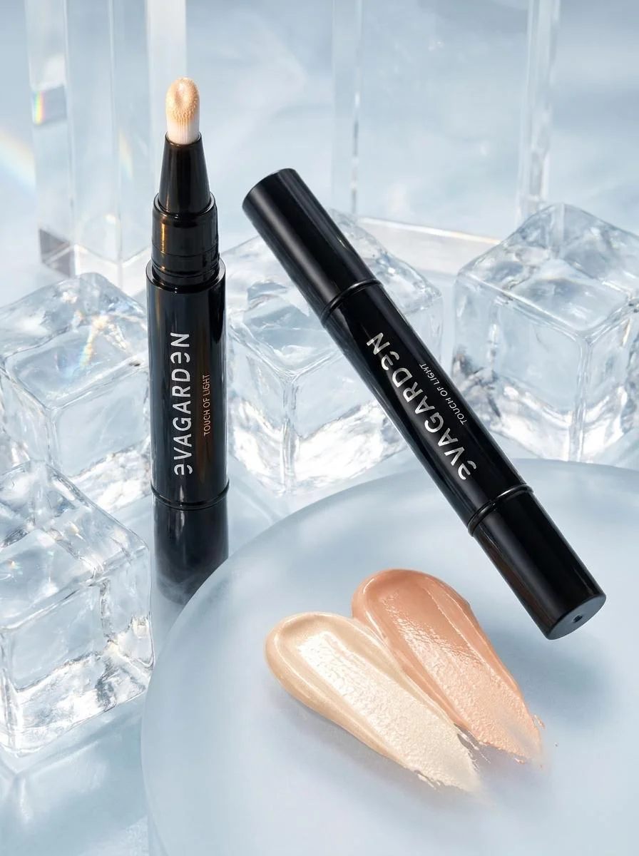 Twee EVAGARDEN Touch of Light twist-pennen naast vloeibare swatches op een glazen achtergrond met ijsblokjes.