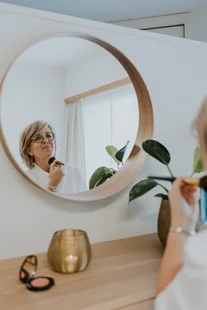 Vrouw bekijkt haar huid in een ronde wandspiegel in het instituut