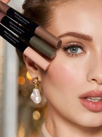 EVAGARDEN Privé Duo Shadow oogschaduw sticks in bruin, groen en roze naast een model met glanzende oogmake-up en barokke pareloorringen.
